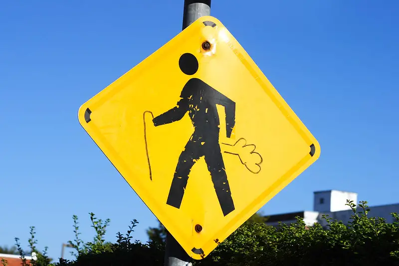 Cross Walk sign vandalized to show man with a cane and gas.